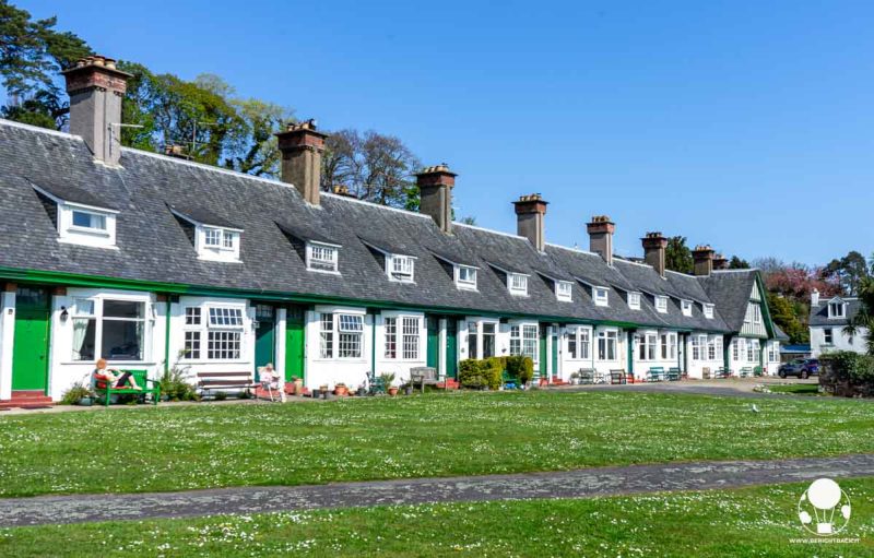 fila di cottage verdi con infissi bianchi e tetti grigi, tutti uguali