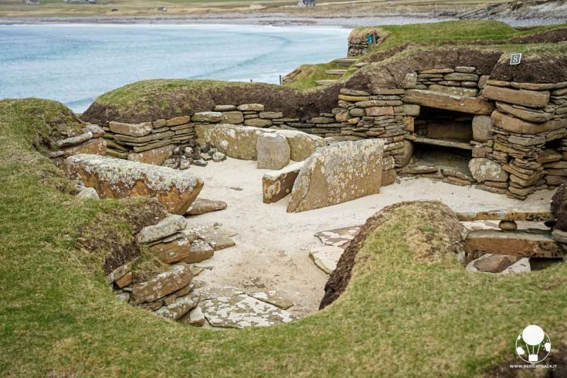 interno di casa preistorica fatto in pietra e scavato nel terreno con il mare sullo sfondo