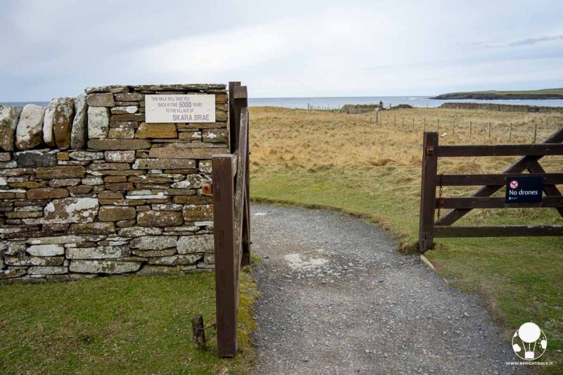 cancello in legno delimitato da un muretto che conduce ad una baia ed un villaggio neolitico